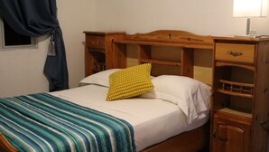 A single bed with a wooden headboard, a bedside table with drawers, and a lamp on the nightstand. - Sunset view suite personal Patio wiew panoramic mountain view and sunset (Trou D'eau Douce)