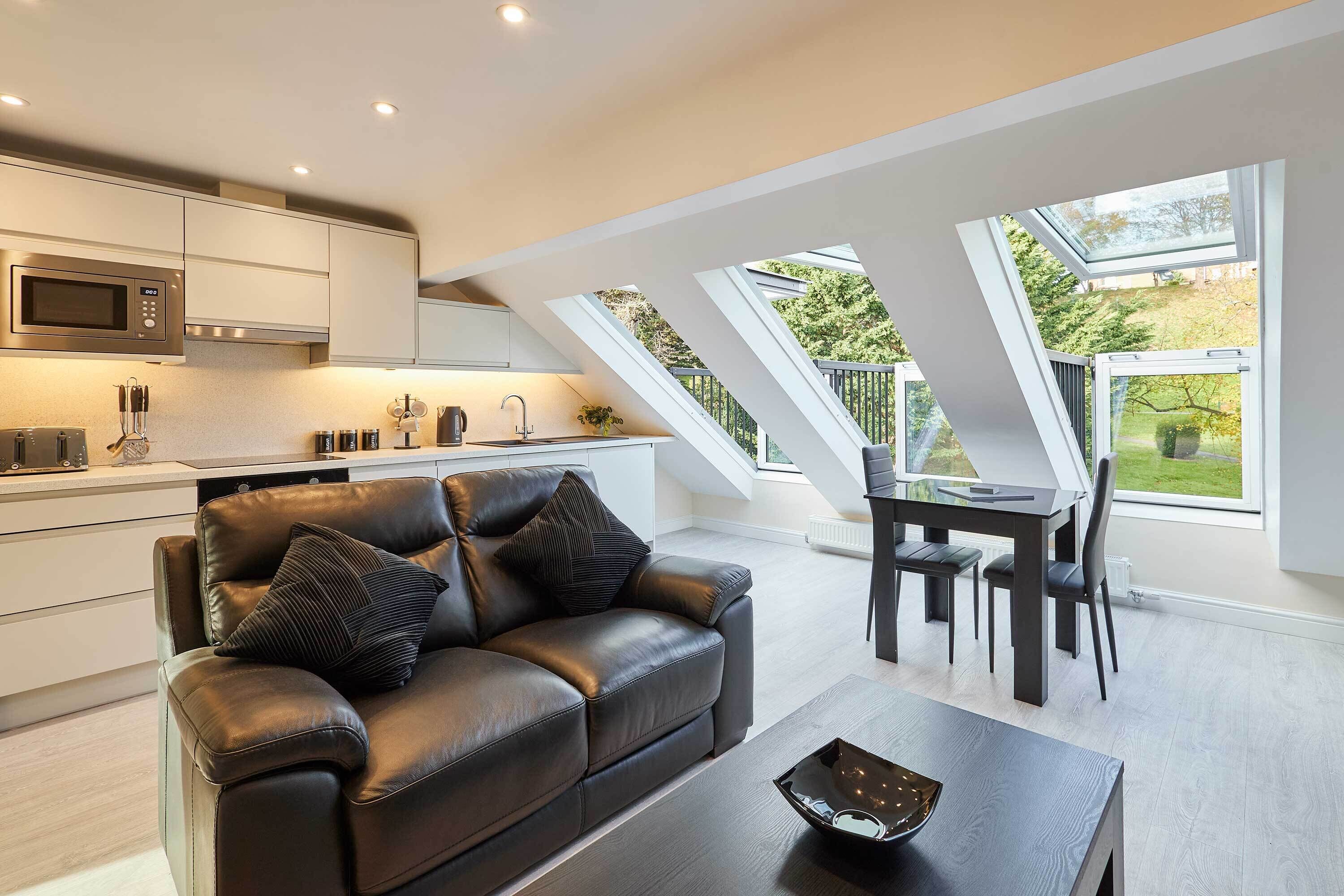 A modern kitchen with a built-in microwave, a dining area with a table and chairs, and a leather sofa with cushions.
