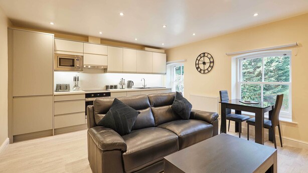 A modern kitchen with a built-in microwave, a dining area with a table and chairs, and a large window with a view of greenery. - Host & Stay | Ross's View, Second Floor, Apartment 4 (Whitby)