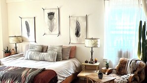 A spacious bedroom with a large bed, a wooden nightstand, a chair, and a window with curtains. - Designer Corner Unit Suite, Cozy 1-bedroom apt, Laundry, AC, (New York)