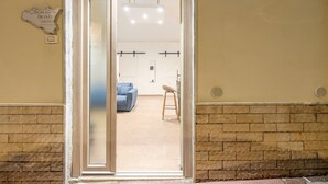 Una puerta abierta que da a una habitación con un sofá azul, un taburete de madera y una pared de piedra.