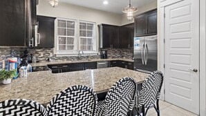 A modern kitchen with dark cabinets, a large island, and a refrigerator. - ⭐Pet Friendly | 4 Bikes | Walk to Beach | Villa Soleil Dunes⭐ (Miramar Beach)