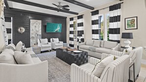 A modern living room with a black and white color scheme, featuring a ceiling fan, striped curtains, and a large TV. - ⭐Pet Friendly | 4 Bikes | Walk to Beach | Villa Soleil Dunes⭐ (Miramar Beach)