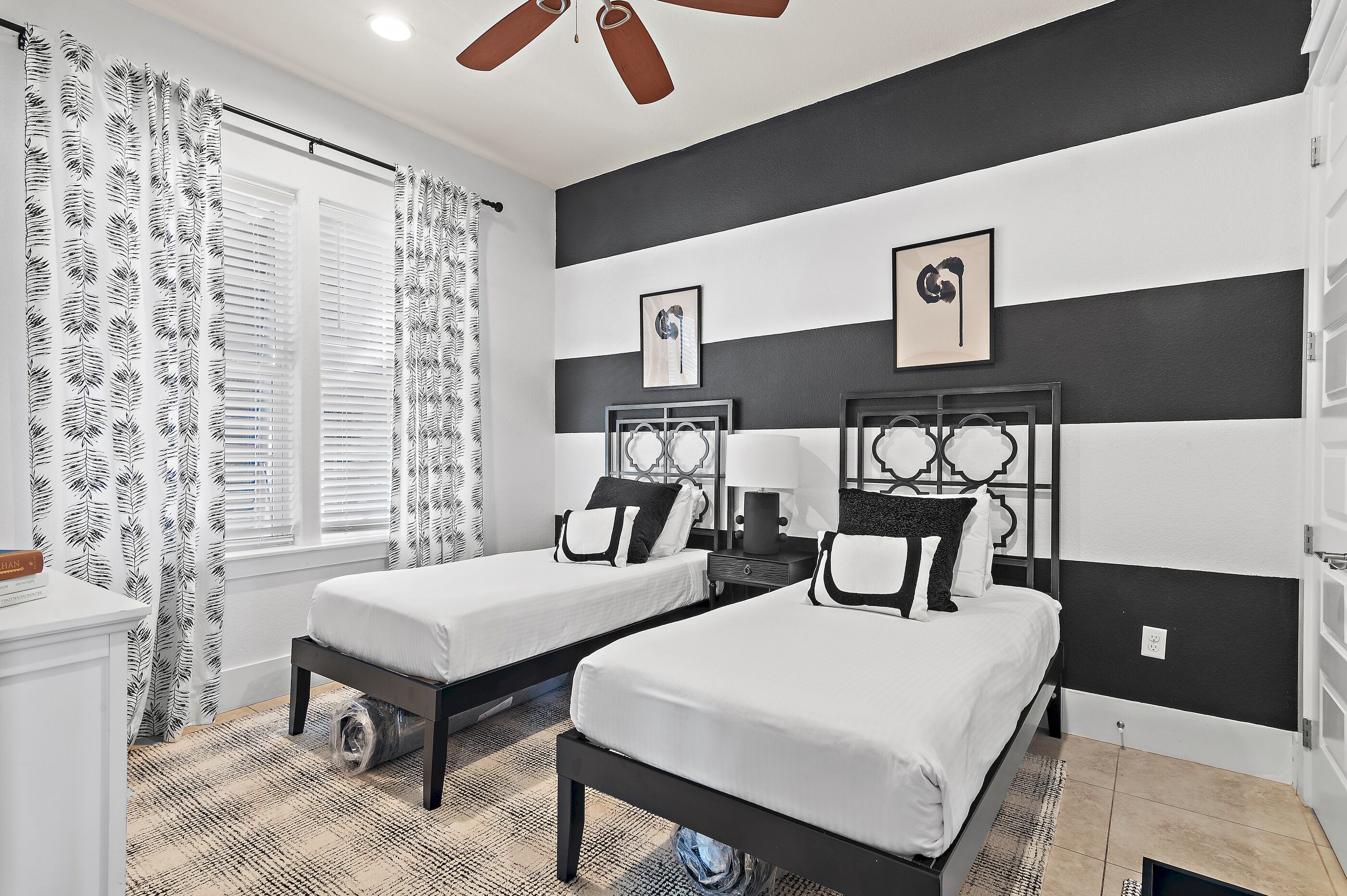 A bedroom with two beds, a ceiling fan, and a window with blinds.