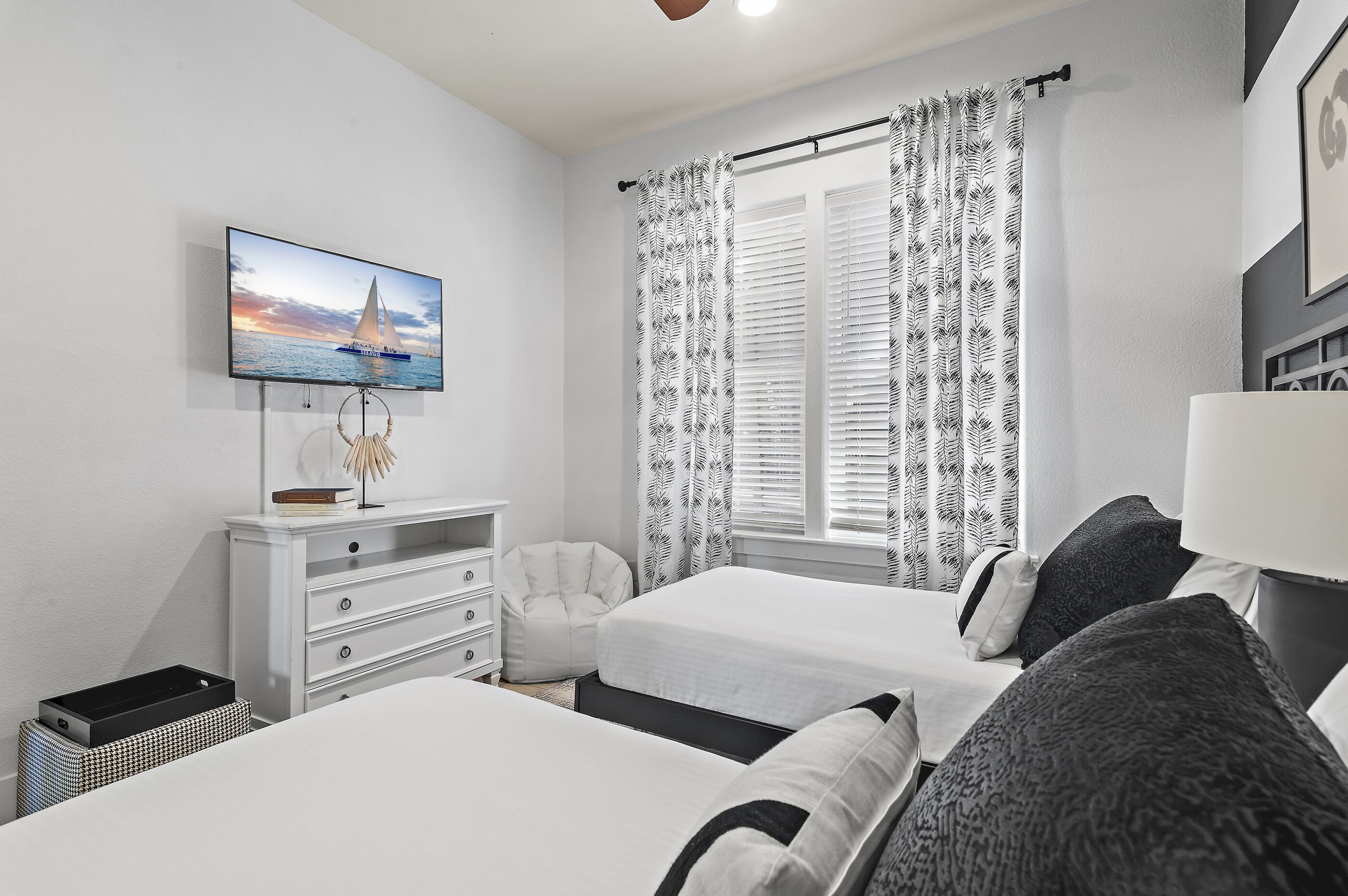Un dormitorio con dos camas, un televisor en la pared, un escritorio con silla y una ventana con cortinas.