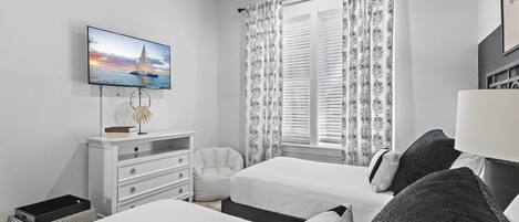 Un dormitorio con dos camas, un televisor en la pared, un escritorio con silla y una ventana con cortinas.