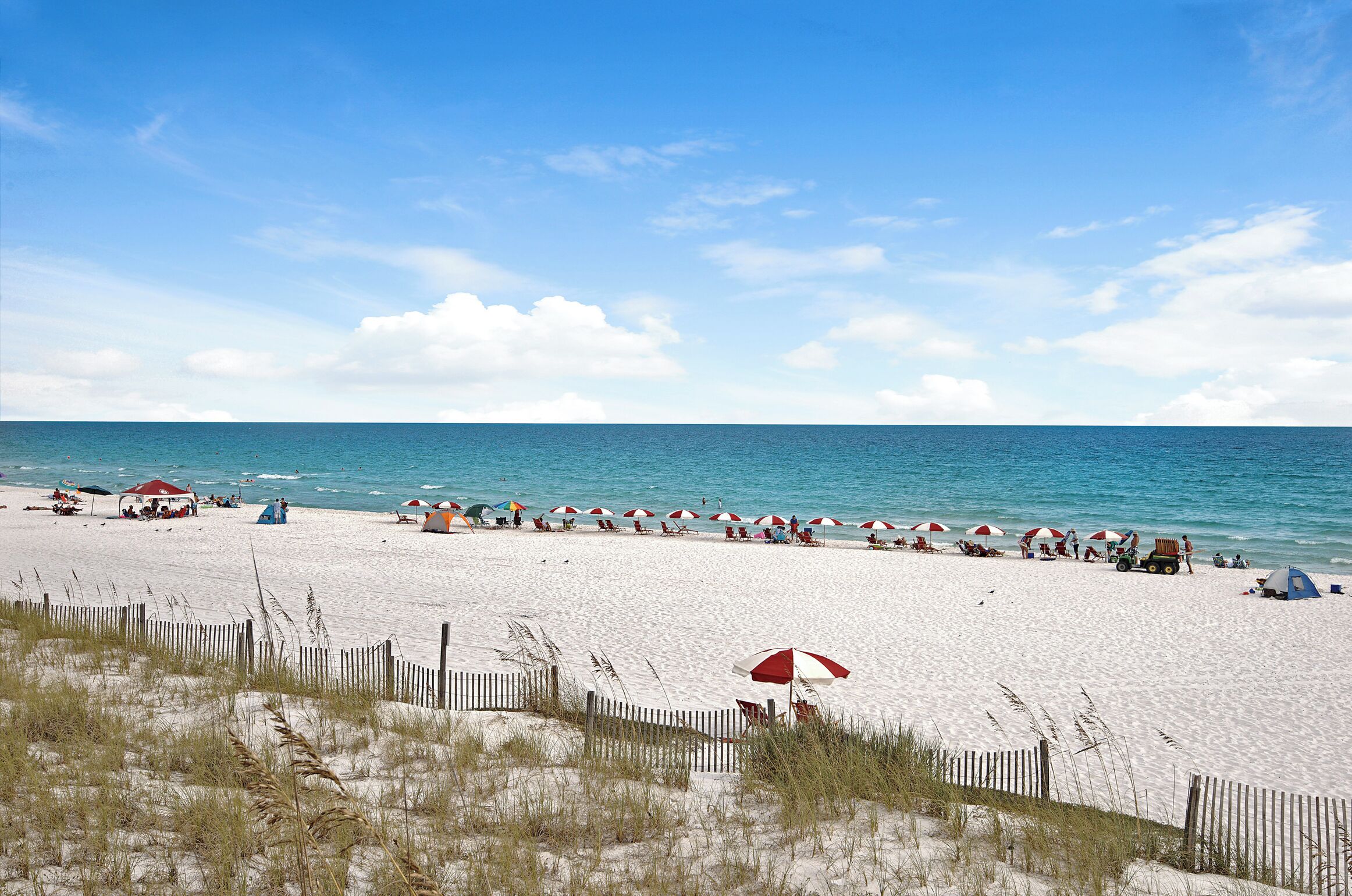 A beach with white sand, red and white umbrellas, and a wooden fence.