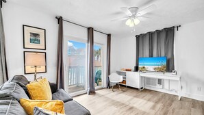 Ein modernes Wohnzimmer mit grauem Sofa, Deckenventilator, Fernseher und großem Fenster mit Vorhängen.