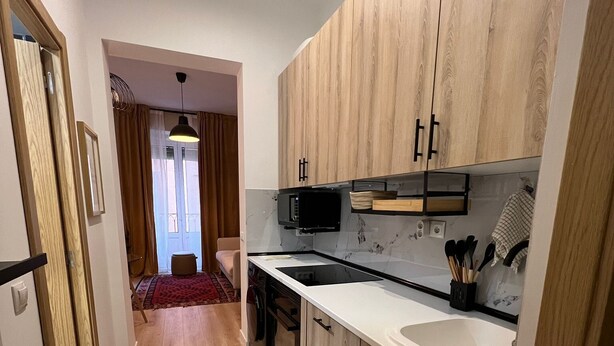 A modern kitchen with wooden cabinets, a white countertop, and a built-in microwave. - w* | Bright 1BR with Balcony in Madrid Centro (Madrid)