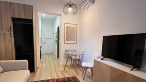 A modern living room with a sofa, a TV, a patterned rug, and a dining area with a table and chairs. - w* | Bright 1BR with Balcony in Madrid Centro (Madrid)