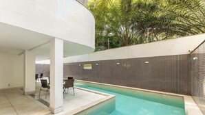 Piscina com parede revestida e área de estar coberta com cadeiras.