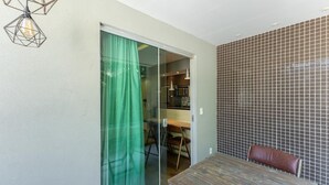 Cozinha moderna com painel de azulejos, área de jantar com mesa e cadeiras de madeira, e porta de vidro deslizante que dá para uma varanda.