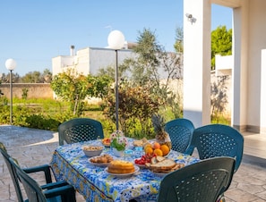 An outdoor dining area with a table set for a meal, surrounded by chairs, with a view of buildings and greenery in the background. - Holiday Home 'Villa Destra' with Private Terrace, Wi-Fi and Air Conditioning (Porto Cesareo)