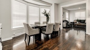 A modern dining area with a dark wooden table and grey upholstered chairs, large windows with blinds, and a dark wood floor. - Stylish & Cozy Apartment with Modern Updates (Kansas City)