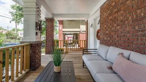 A covered porch with a brick wall, a wooden bench, a gray sofa, and a potted plant. - Stylish & Cozy Apartment with Modern Updates (Kansas City)