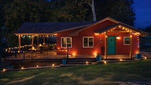 A red house with a porch, string lights, and a green door.