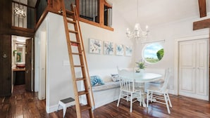 A dining area with a white table and chairs, a chandelier, and a view of the outdoors through a circular window.