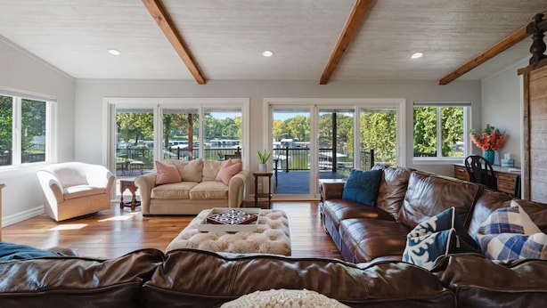 A spacious living room with a high ceiling, large windows, and a view of a lake.