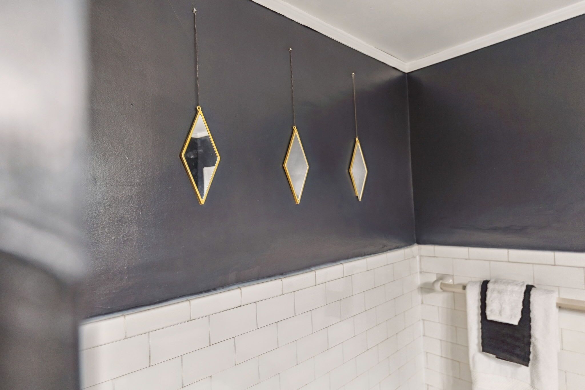 Un baño con paredes oscuras, suelo de baldosas blancas y tres adornos en forma de diamante.