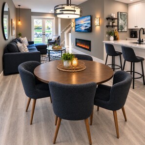 A modern living room with a round dining table, dark upholstered chairs, a fireplace, and a kitchen area with bar stools. - #2 Executive Townhome at Sunrise Ridge Resort. Sleep 6. Seasonal Pool / HotTub. (Parksville)