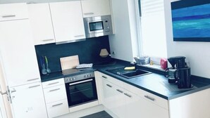 A modern kitchen with white cabinets, a black countertop, a microwave, an oven, and a coffee maker.