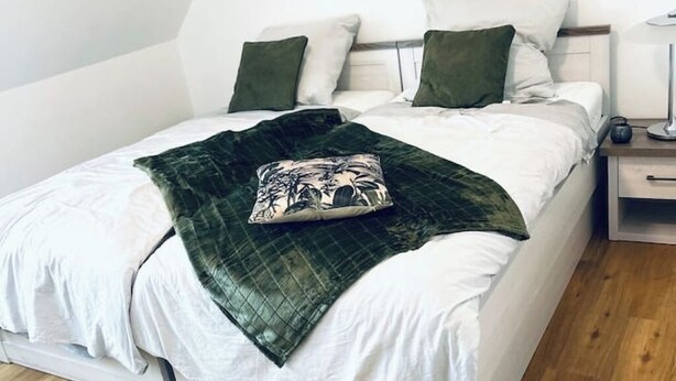 A neatly made bed with white bedding and a green throw blanket, a bedside table with a lamp, and a nightstand with a lamp.