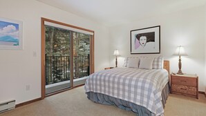 A bedroom with a large bed, two bedside lamps, a nightstand, a window with a view of trees, and a framed picture on the wall. - I1 Gore Creek Meadows -Gorgeous Mountain Home, Private Hot Tub! (Vail)