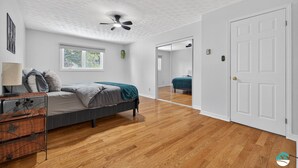 Un dormitorio con cama, mesita de noche, lámpara, ventana y ventilador de techo.