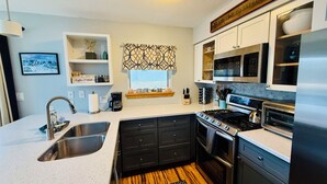 A modern kitchen with a stainless steel sink, black cabinets, a stove, and a microwave. - Stunning Pet Friendly House with Pond View, Sauna and Jetted Tub in the Home (Killington)