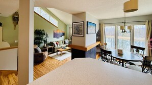 A spacious living area with a large window, a dining table, and a sofa. - Stunning Pet Friendly House with Pond View, Sauna and Jetted Tub in the Home (Killington)