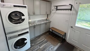 Une petite buanderie comprenant deux machines à laver, un plan de travail, des placards, un banc et une porte avec une fenêtre.