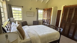 Een slaapkamer met een bed, een plafondventilator, een nachtkastje met een lamp en een raam met gordijnen.