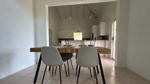 Een eetgedeelte met een houten tafel en vier stoelen, dat uitkomt op een keuken met witte kastjes en een raam.