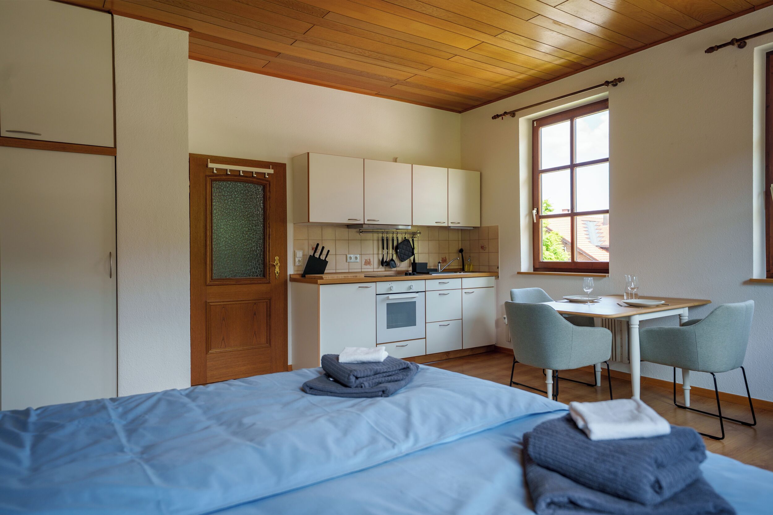 Ein Zimmer mit einem Bett, einem Esstisch mit Stühlen, einer Küchenzeile und einem Fenster.
