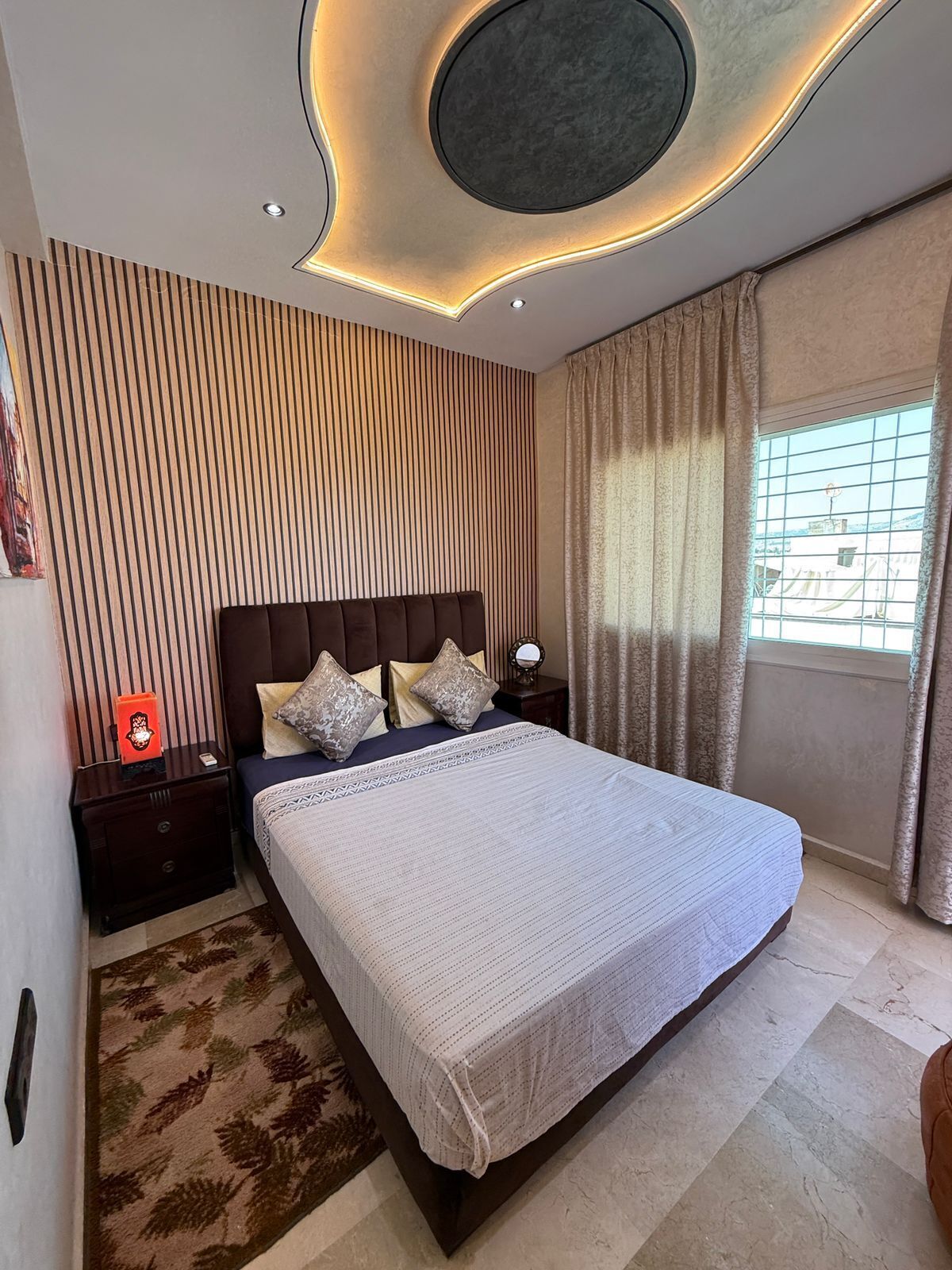 A modern bedroom with a large bed, wooden panel wall, and a window with curtains.