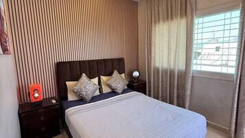 A modern bedroom with a large bed, wooden panel wall, and a window with curtains.