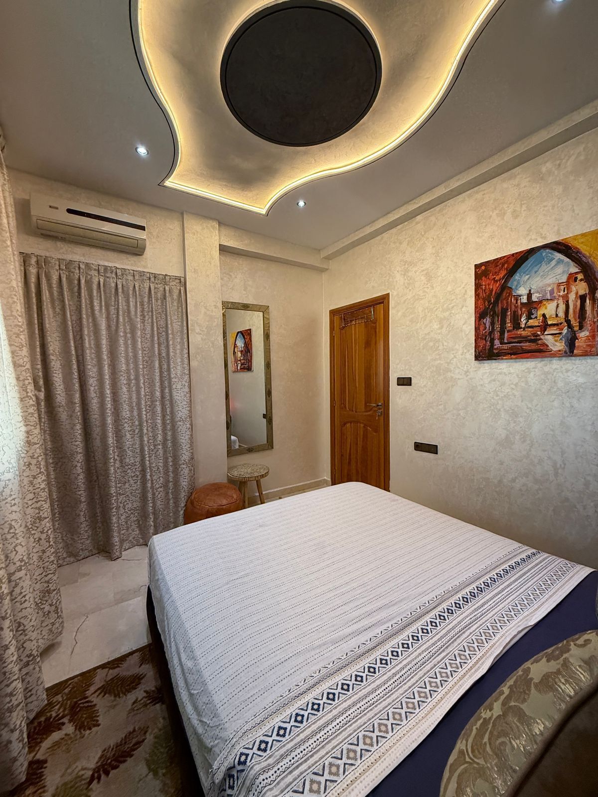 Een slaapkamer met een bed, een houten deur, een schilderij, een airconditioner en een gordijn.