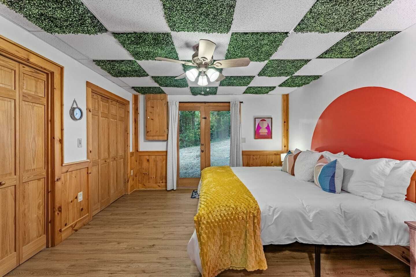 A bedroom with a bed, wooden wardrobe, a ceiling fan, and a view through a door.