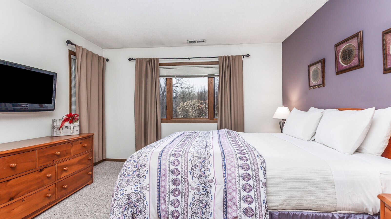 A bedroom with a bed, a dresser, a TV, and a window with curtains.