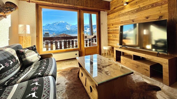 Un soggiorno con divano, televisore, pareti in legno e vista sulle montagne.
