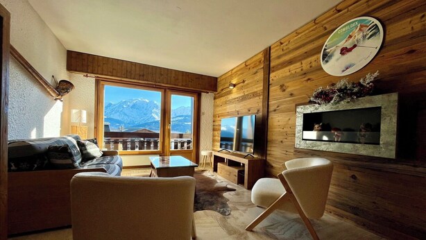 A modern living room with a large window, wooden walls, a flat-screen TV, and a cozy seating area. - The Balcony of the Giant in Combloux (Combloux)