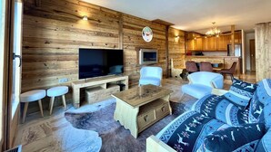 Interno di una baita in legno con soggiorno, televisione, posti a sedere e angolo cottura.