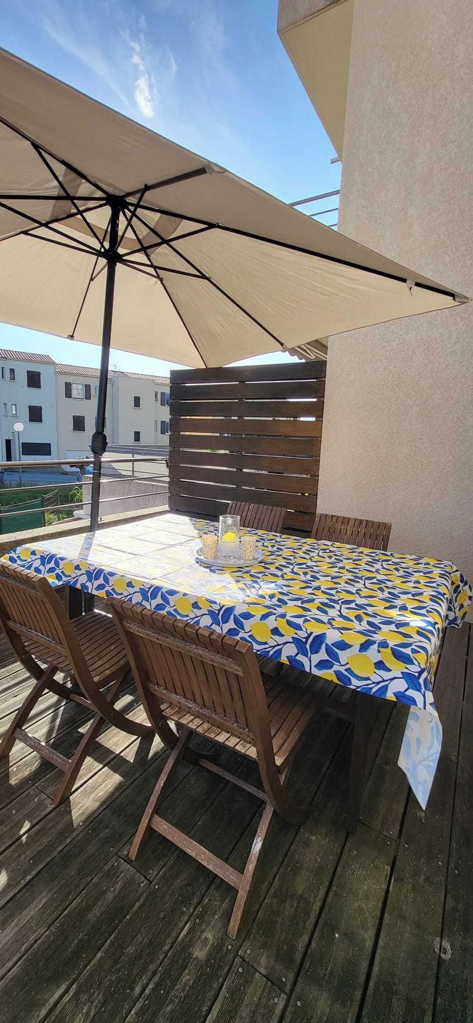 Eine Terrasse im Freien mit Tisch, bedeckt mit einer gemusterten Tischdecke, umgeben von Holzsesseln.