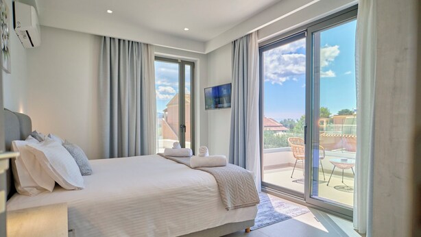 Un dormitorio moderno con una cama grande, televisión y balcón con mobiliario exterior.