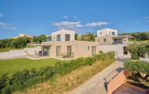 A modern house with a stone facade, a paved driveway, and a well-maintained lawn. - Arillas Villas Dinos (Corfu)