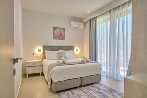 A modern bedroom with a large bed, bedside tables, a painting, and a window with curtains. - Arillas Villas Dinos (Corfu)