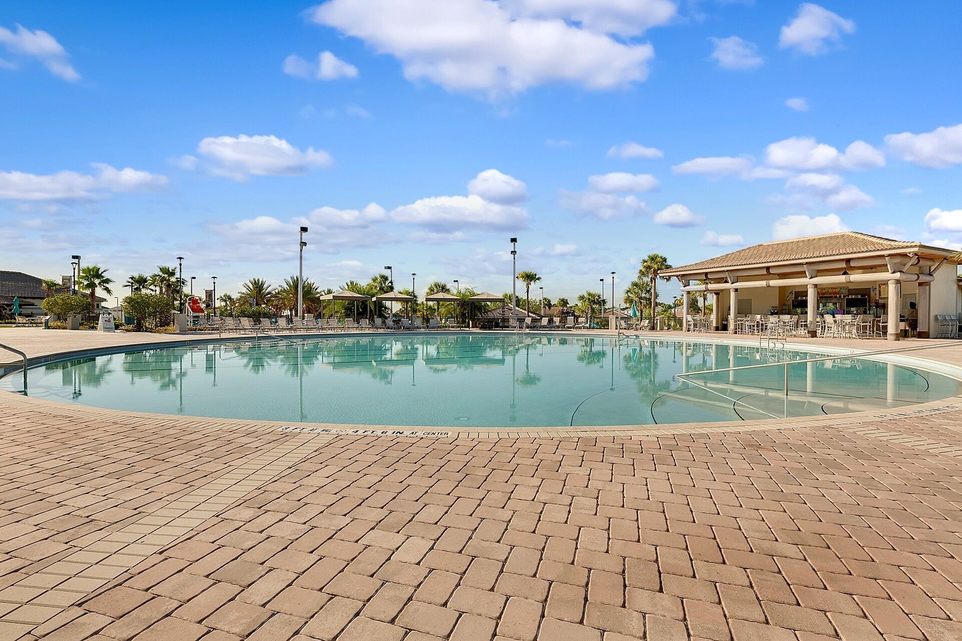 Una piscina con sillones de descanso y sombrillas, rodeada de palmeras y una zona de estar cubierta.
