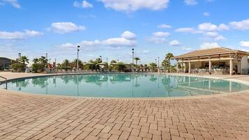 Una piscina con sillones de descanso y sombrillas, rodeada de palmeras y una zona de estar cubierta.