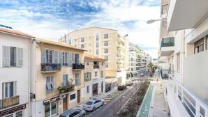 Una calle estrecha en la ciudad con edificios de varios pisos, coches aparcados y un carril bici verde.