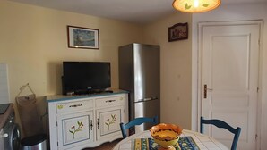 Habitació amb televisió sobre un moble, nevera, taula de menjador amb cadires i una porta.